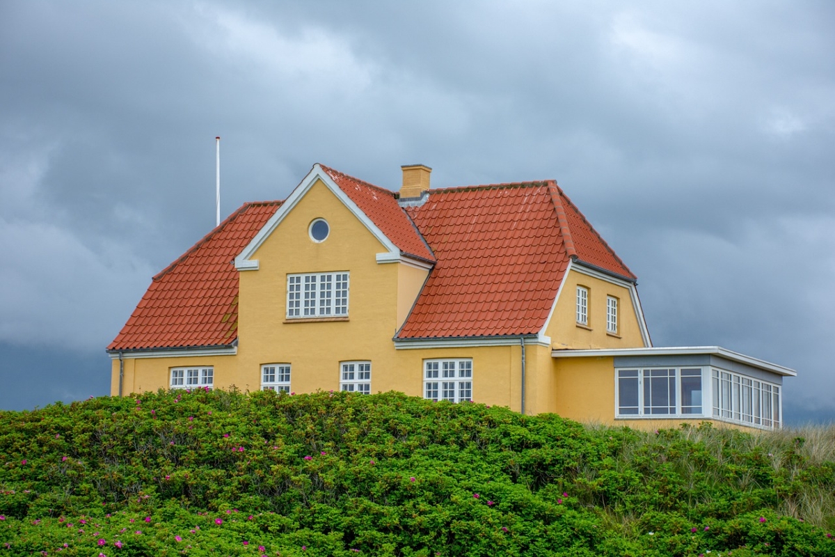 Eines der modernen Häuser mit Dachgeschoss, gelb gestrichen, mit rotem Dach, bewachsen mit Grünzeug und Blumen.