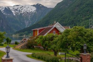 Tradycyjne domy stalowe w odmianach, z czerwonymi dachówkami, malowniczo położone wśród norweskich gór i zieleni blisko jeziora.