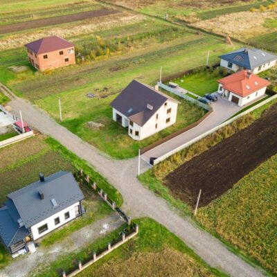 Obraz lotniczy przedstawiający proces budowy energooszczędnego domu stalowego na tle wiejskiego krajobrazu.