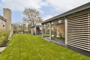 Ein modernes Haus mit großen Fenstern vor einer Gartenkulisse, bei dem die gesetzlichen Anforderungen an den Stahlhausbau erfüllt wurden.